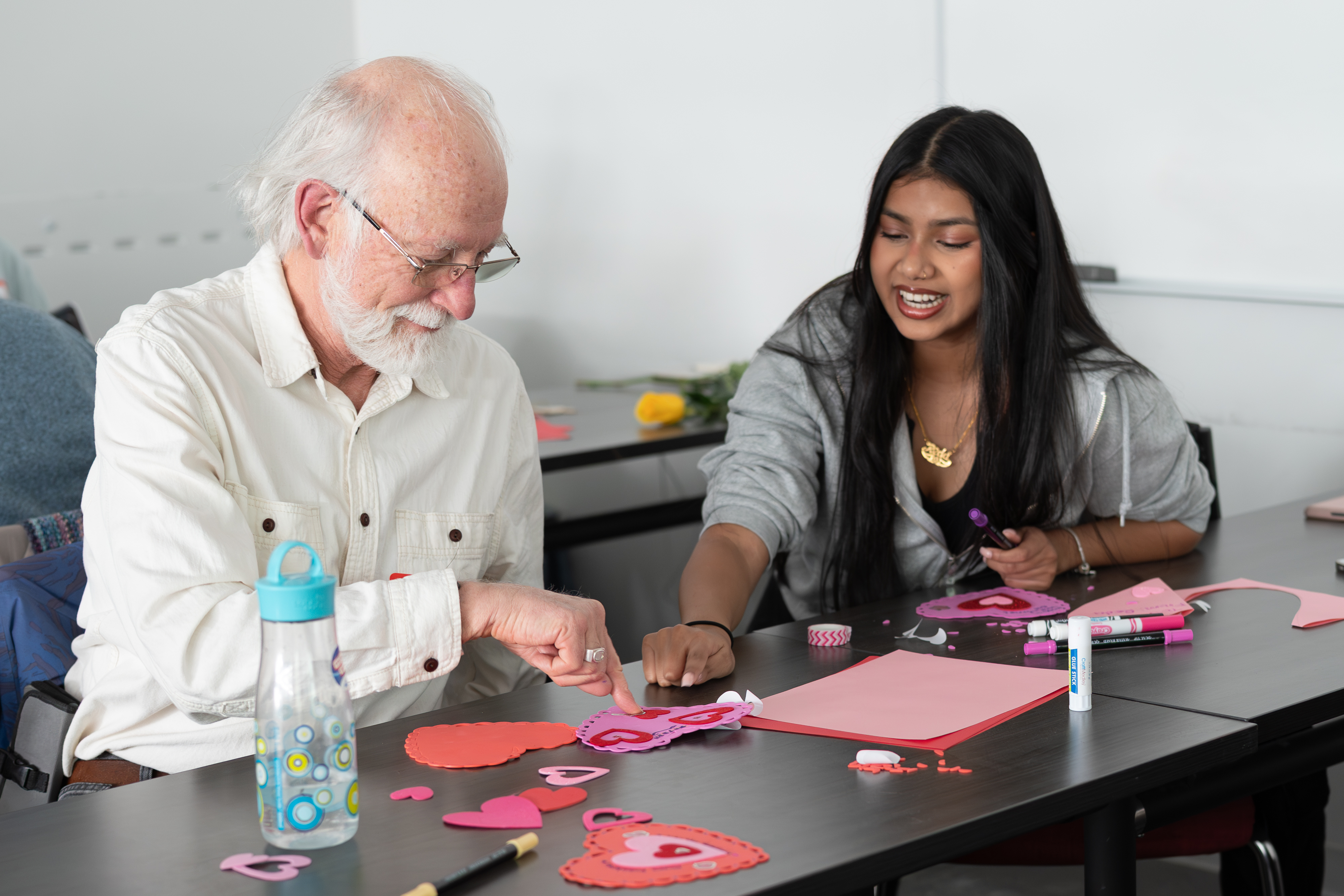 An elderly man makes Valentines with a student